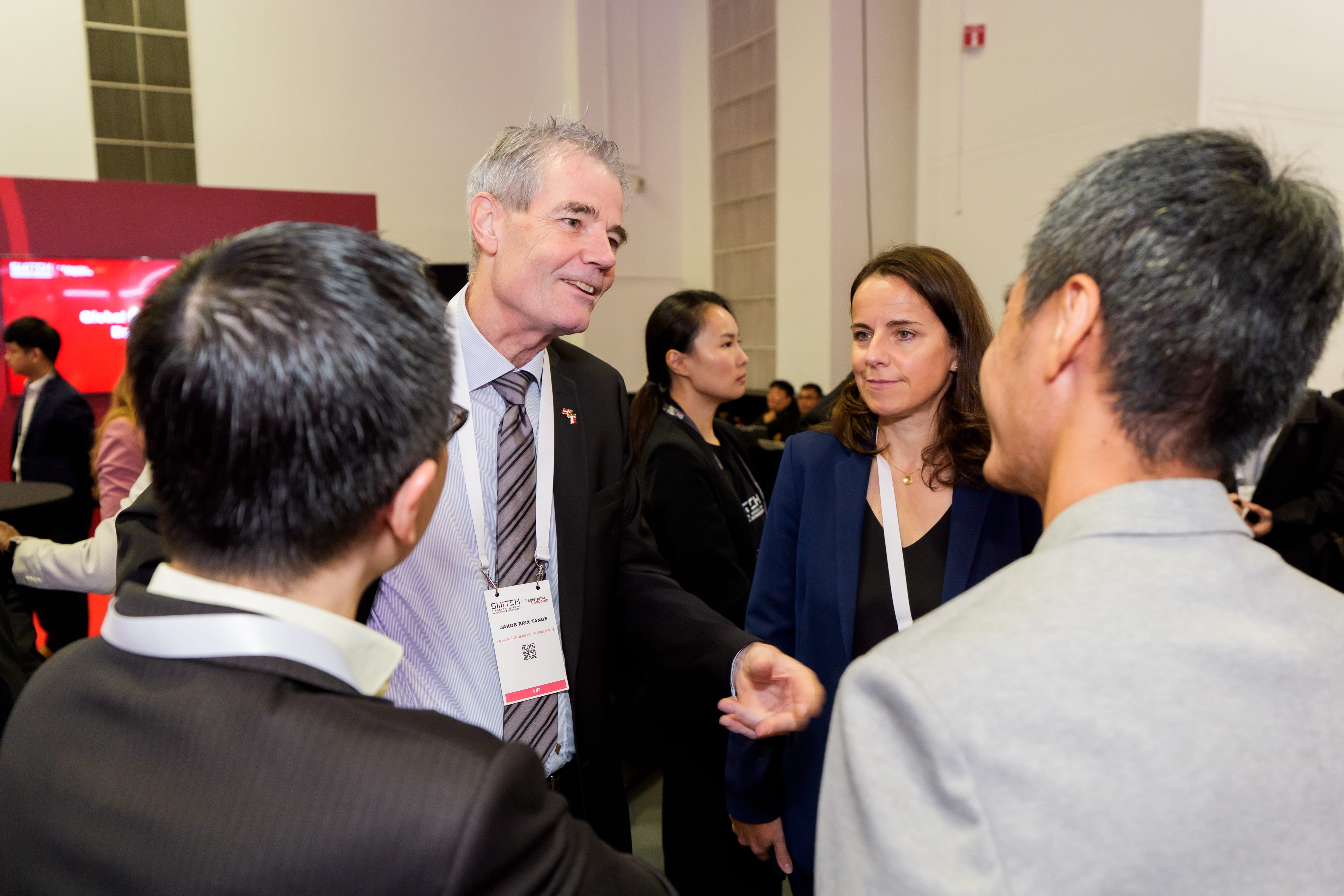 A photograph of a man and woman in the centre of the frame talking with the people in the foreground.